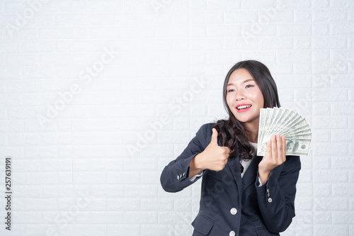 A young businesswoman holds a dollar note on a white brick wall background. photo