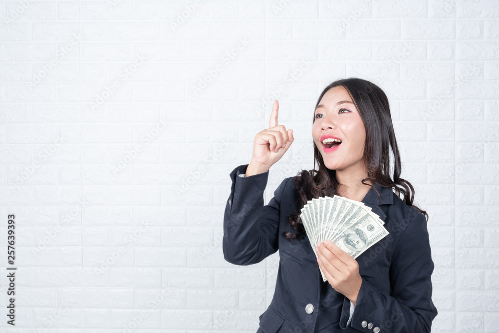 A young businesswoman holds a dollar note on a white brick wall background. A young businesswoman holds a dollar note on a white brick wall background.