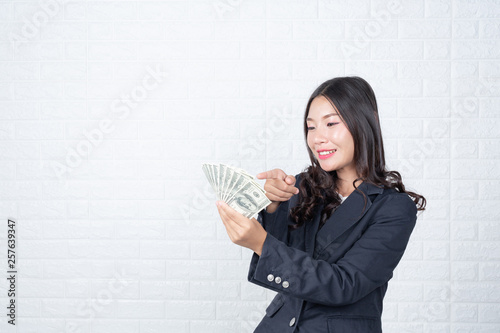 A young businesswoman holds a dollar note on a white brick wall background. photo