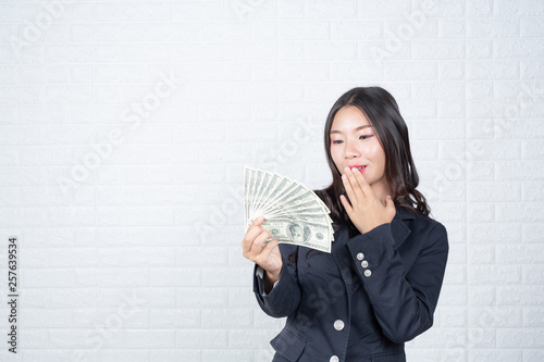 A young businesswoman holds a dollar note on a white brick wall background. photo