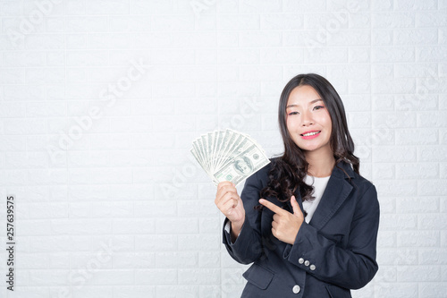 A young businesswoman holds a dollar note on a white brick wall background. photo