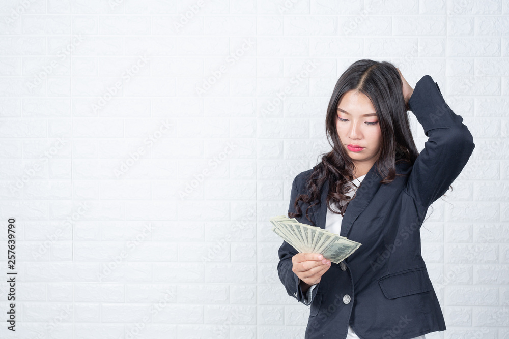 A young businesswoman holds a dollar note on a white brick wall background. A young businesswoman holds a dollar note on a white brick wall background.