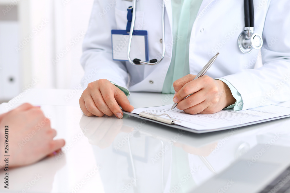 Unknown doctor woman consulting patient while filling up an application form at the desk in hospital. Just hands close-up. Medicine and health care concept Unknown doctor woman consulting patient while filling up an application form at the desk in hospital. Just hands close-up. Medicine and health care concept