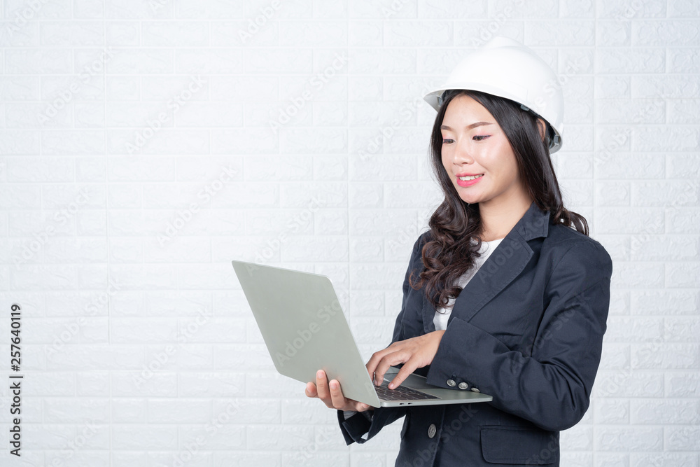 Engineering woman holding a separate notebook, white brick wall Made gestures with sign language. Engineering woman holding a separate notebook, white brick wall Made gestures with sign language.