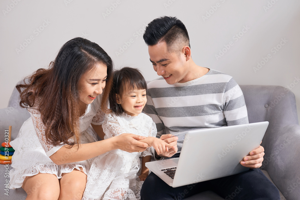 Parents and daughter playing together with a laptop on a couch Parents and daughter playing together with a laptop on a couch