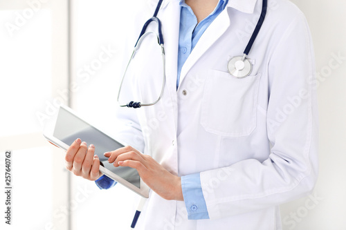 Woman doctor using tablet computer while standing straight in hospital closeup. Healthcare, insurance and medicine concept