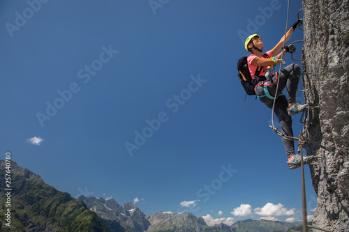 Pretty, female climber on a via ferrata - climbing on a rock in Swiss Alps