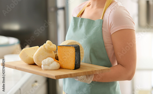 Woman holding board with assortment of tasty cheese in kitchen photo