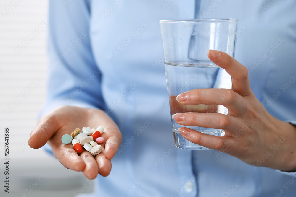 Young unknown woman holding pills and glass of water, closeup of hands. Medicine and healthcare concept Young unknown woman holding pills and glass of water, closeup of hands. Medicine and healthcare concept