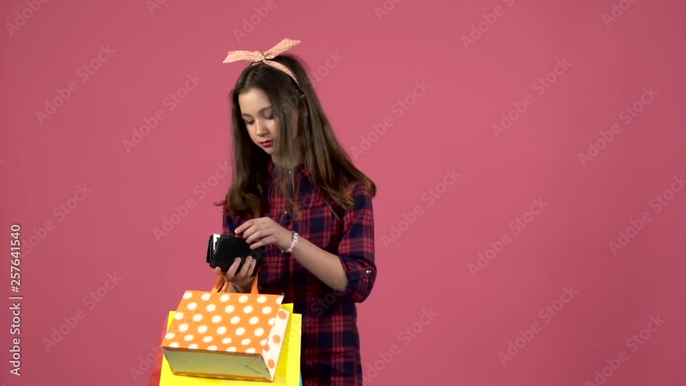 Girl looks into shopping bags then the purse has run out of money but there is a card. Pink background. Slow motion Girl looks into shopping bags then the purse has run out of money but there is a card. Pink background. Slow motion
