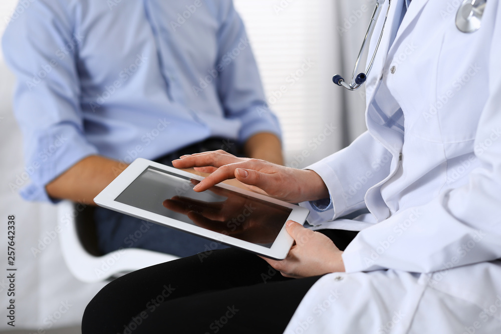 Female doctor using touchpad or tablet computer while consulting man patient in hospital. Medicine and healthcare concept Female doctor using touchpad or tablet computer while consulting man patient in hospital. Medicine and healthcare concept