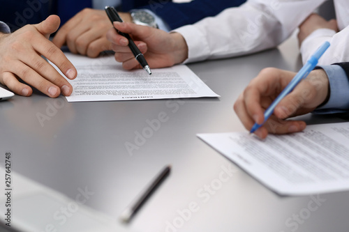 Group of business people and lawyer discussing contract papers sitting at the table, closeup. Businessman is signing document after agreement done