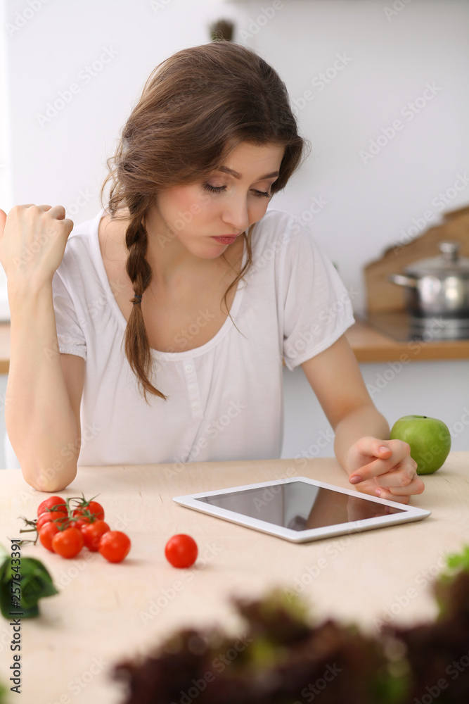 Young  woman looking for a new recipe for  cooking in a kitchen. Housewife is making online shopping by tablet computer and credit card