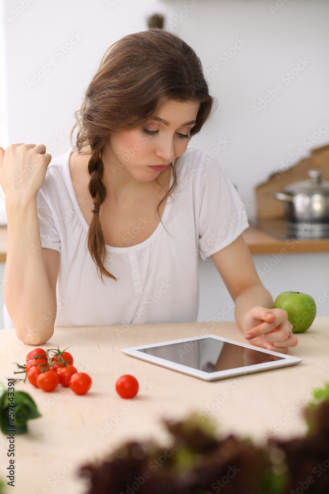 Young woman looking for a new recipe for cooking in a kitchen. Housewife is making online shopping by tablet computer and credit card Young woman looking for a new recipe for cooking in a kitchen. Housewife is making online shopping by tablet computer and credit card