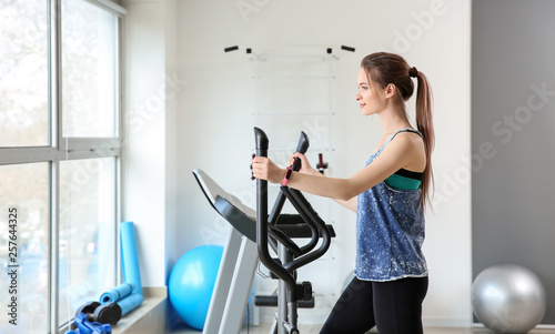 Sporty young woman training on machine in gym