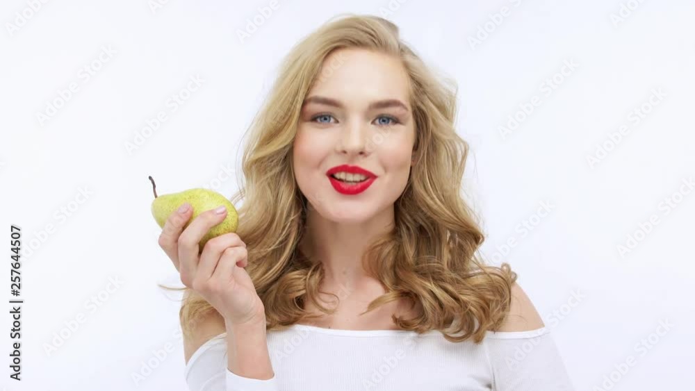 Young beautiful woman eating fruit and says yum. Happy adult girl eats pear. VIdeo footage of a blond caucasian woman eats fruits over white background. 4k resolution. Young beautiful woman eating fruit and says yum. Happy adult girl eats pear. VIdeo footage of a blond caucasian woman eats fruits over white background. 4k resolution.