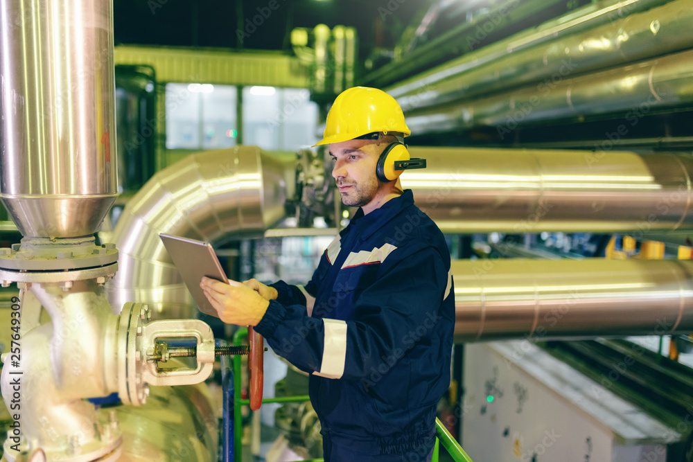 © Dusan Petkovic - Caucasian serious hardworking worker in protective suit and helmet on head using tablet while standing in heavy industry plant. © Dusan Petkovic - Caucasian serious hardworking worker in protective suit and helmet on head using tablet while standing in heavy industry plant.