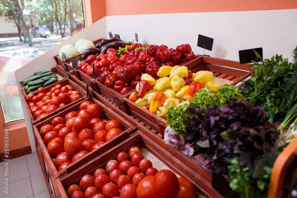 Tomatoes, peppers, eggplants, cabbage, cucumbers and greens in boxes on a shelf in a vegetable store