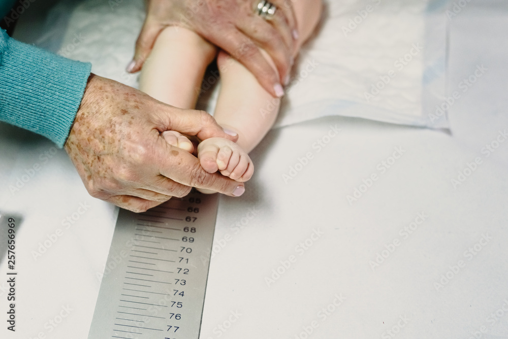 newly born in the clinic of the pediatrician measuring a height and height of the baby with the help of a ruler. - obrazy, fototapety, plakaty 