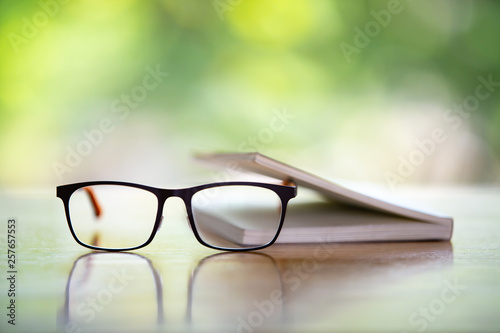 Black eyeglasses with a book on wooden table, Bokeh garden background, Close up & Macro shot, Selective focus, Stationery concept