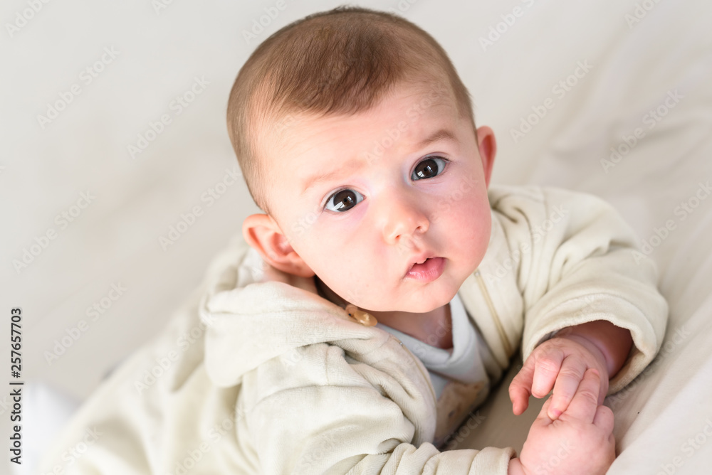 Beautiful and sweet newborn baby lying face down on the bed raising his head to look at the camera curiously.