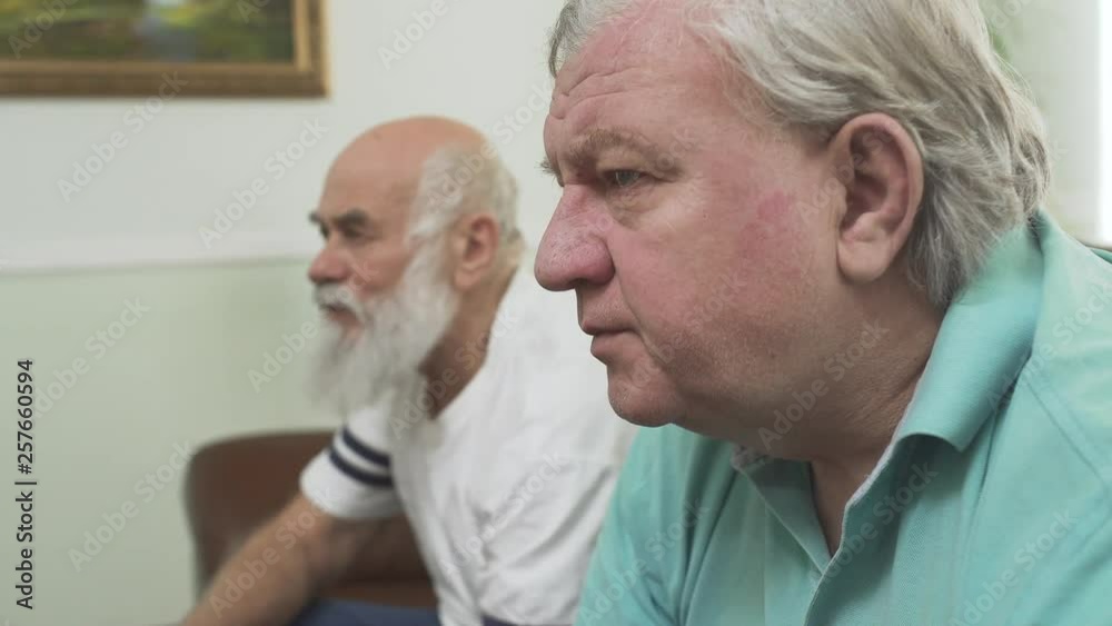 Close up of two mature senior men watching TV at home. Friends watching football soccer while eating chips. People involved in game Close up of two mature senior men watching TV at home. Friends watching football soccer while eating chips. People involved in game