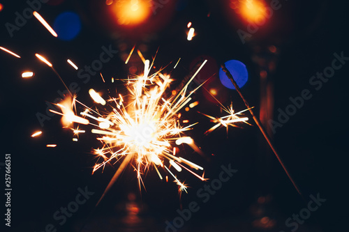 sparkling Bengal sparklers sticks in flames on a black background with lights bokeh. christmas theme new year background. holiday card