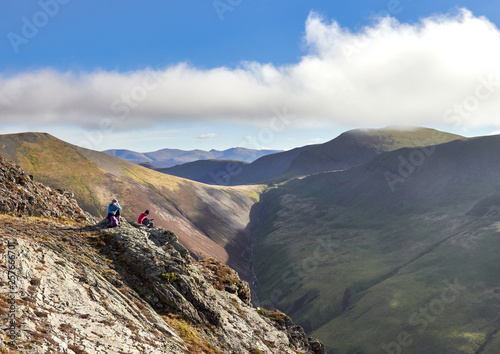 Two hikers sitting down on a rocky crag with distant views of Sand Hill and Crag Hill above Gasgale Gill in the English Lake District, UK. photo