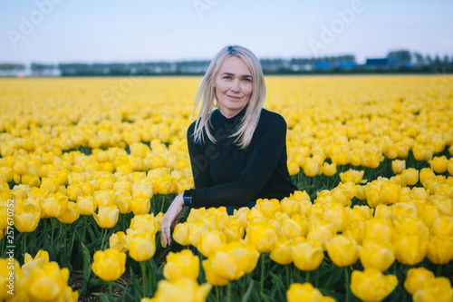 Beautiful young blond hair woman sit between of the yellow tulips field in Amsterdam region, Holland, Netherlands. Lovely spring concept. photo