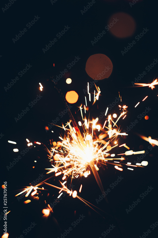 Obraz premium sparkling Bengal sparklers sticks in flames on a black background with lights bokeh. christmas theme new year background. holiday card
