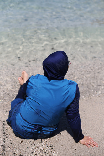 A Muslim woman is bathing on a beach in a traditional full body closed swimsuit. Religious restrictions lifestyle. 
