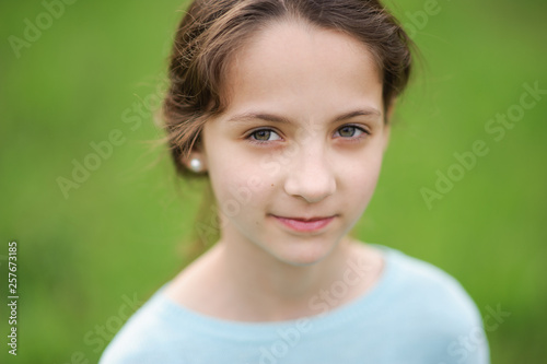 portrait of happy beautiful little caucasian girl in blue blouse on green outdoor background