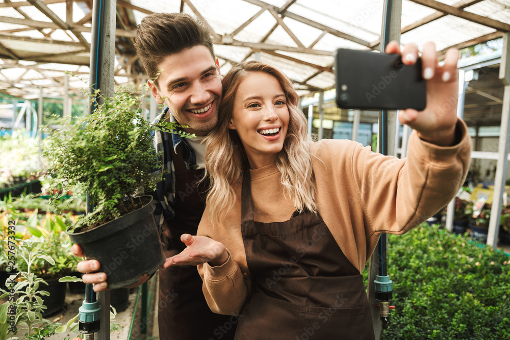 Emotional happy young two colleagues gardeners at the workspace over plants take a selfie by mobile phone.