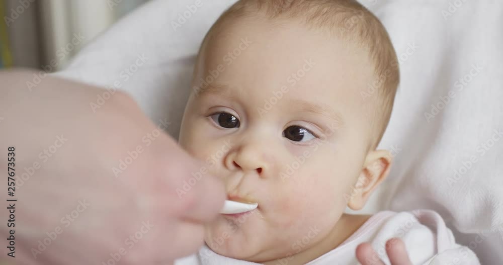 Closeup shot of mom feeds her little 8 months old baby from a spoon Closeup shot of mom feeds her little 8 months old baby from a spoon