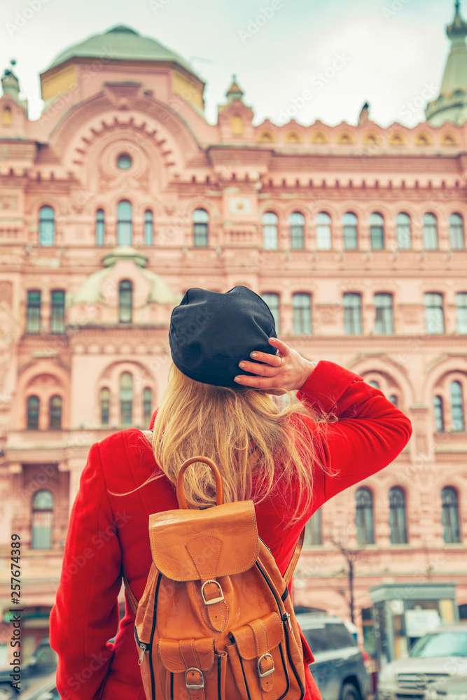 Woman in a red coat and a black cap looks at a beautiful pink house.