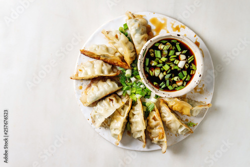 Fotografie Fried asian dumplings Gyozas potstickers in white ceramic plate served with bowl of soy onion sauce over white marble background