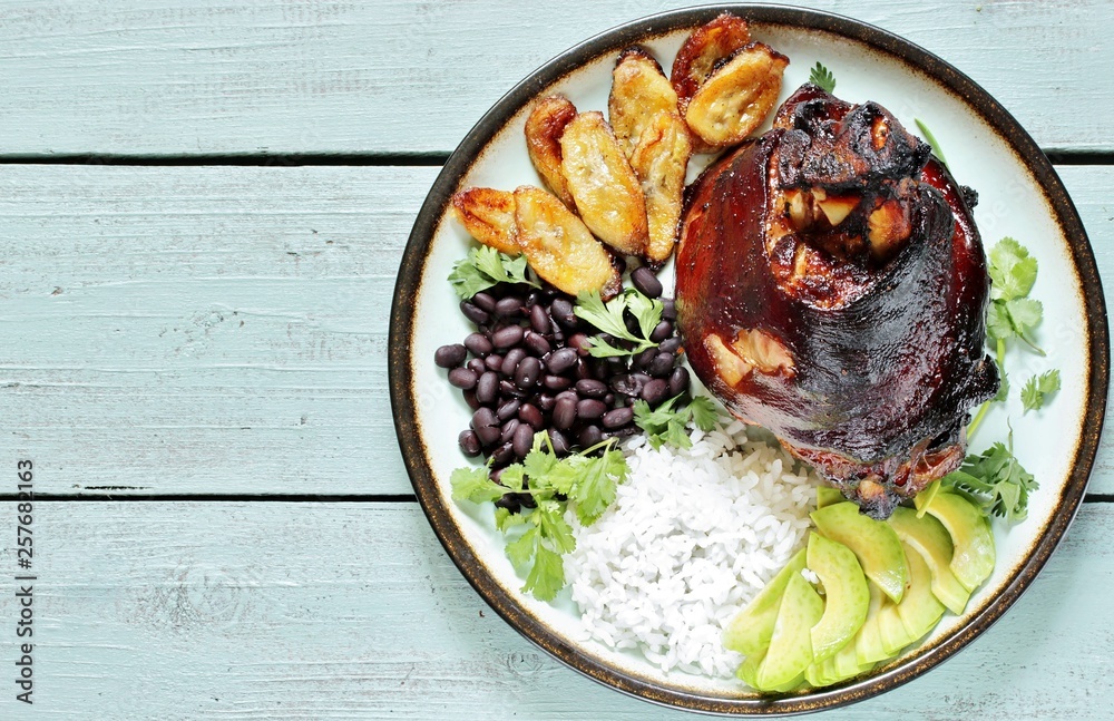 buddha bowl in latin american style. Colombian traditional food. pork knuckle ham baked, rice, black beans, fried bananas, avocado, cilantro. copy space. top view.