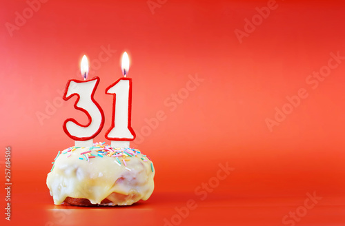 Thirty one years birthday. Cupcake with white burning candle in the form of number 31. Vivid red background with copy space