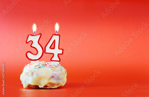 Thirty four years birthday. Cupcake with white burning candle in the form of number 34. Vivid red background with copy space photo