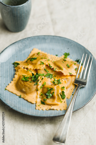 Homemade Italian ravioli pasta with parsley on a blue ceramic plate.