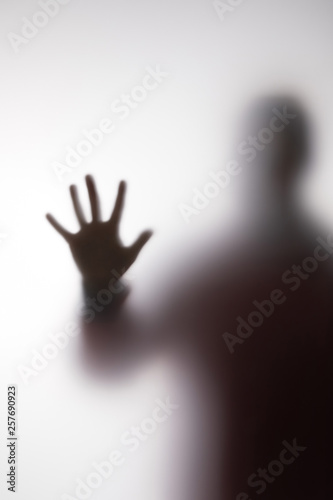 Blurry silhouette of person touching glass with hand