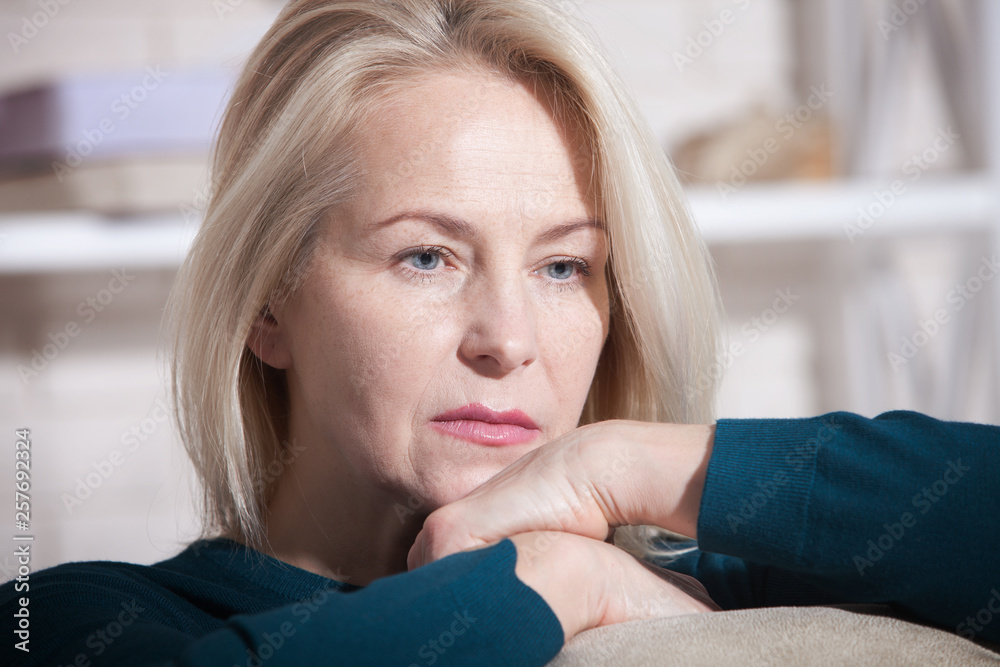 Sad woman sitting on a sofa in the living room Sad woman sitting on a sofa in the living room