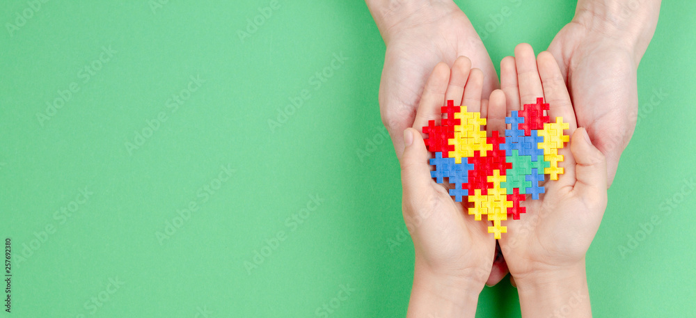 Adult and kid hands holding colorful heart on green background. World autism awareness day concept