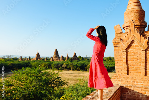 girl stands on rim of Myanmar pagoda ruin, back to camera, looks into view far away, at Bagan, Myanmar