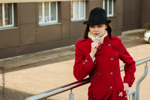 Beautiful young girl in a red coat holding glasses in her hands