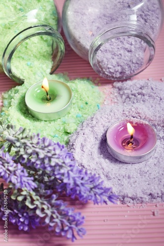 Lilac and green bath salt and candles on pink background.