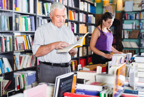 Old male is choosing book for reading in free time in bookstore.