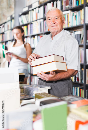 Old male is showing book that he bought in bookstore.