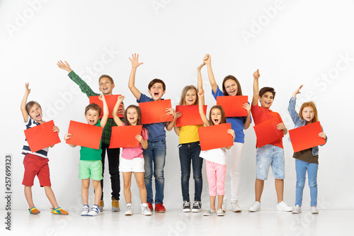 Group of happy screaming children with a red empty banners isolated in white studio background. Education and advertising concept