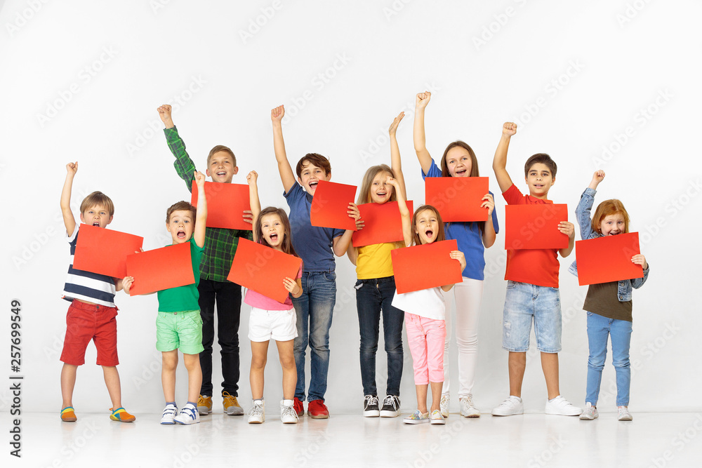 Obraz premium Group of happy screaming children with a red empty banners isolated in white studio background. Education and advertising concept